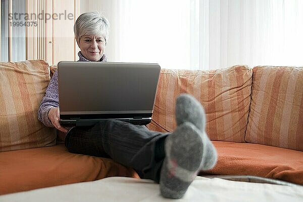 Frau sitzt mit einem Laptop auf der Couch