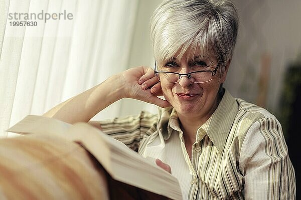 Vergnügte Seniorin sitzt mit einem Buch auf der Couch