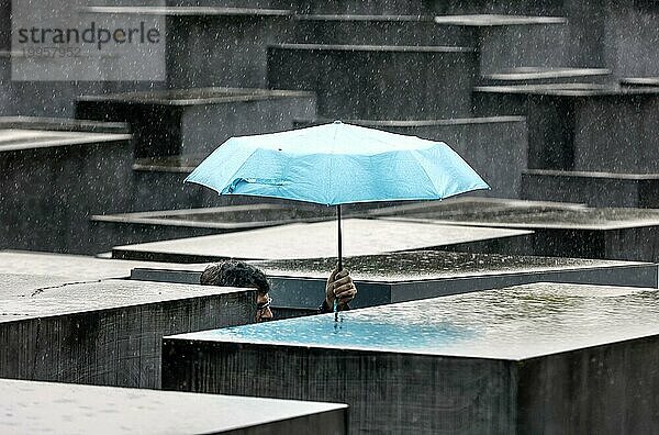 Ein Besucher des Denkmals für die ermordeten Juden Europas schützt sich mit einem Regenschirm vor starkem Regenfall  Berlin  23.06.2023