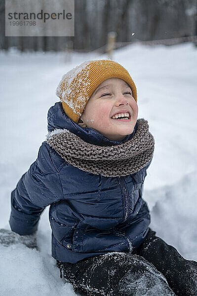 Junge sitzt im Schnee und lacht im Winterpark