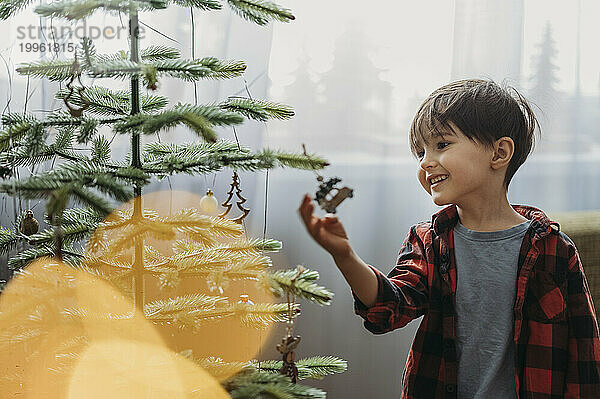 Lächelnder Junge schmückt zu Hause den Weihnachtsbaum