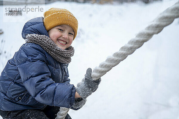 Lächelnder Junge zieht Seil im Winterpark