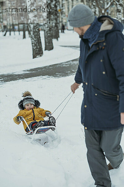 Father sledding son in winter park
