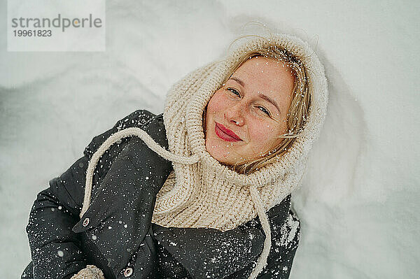 Glückliche junge Frau  die auf Schnee liegt