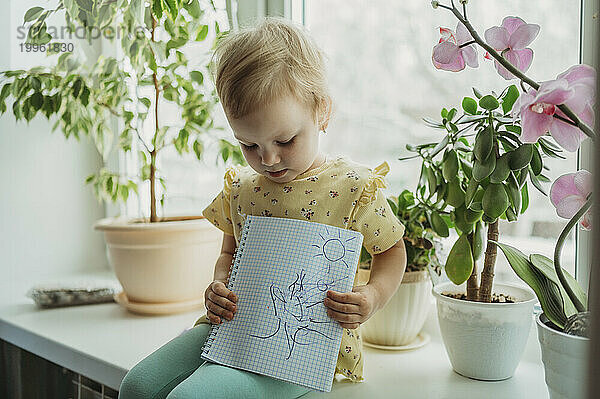 Mädchen sitzt auf der Fensterbank und zeigt Zeichnung