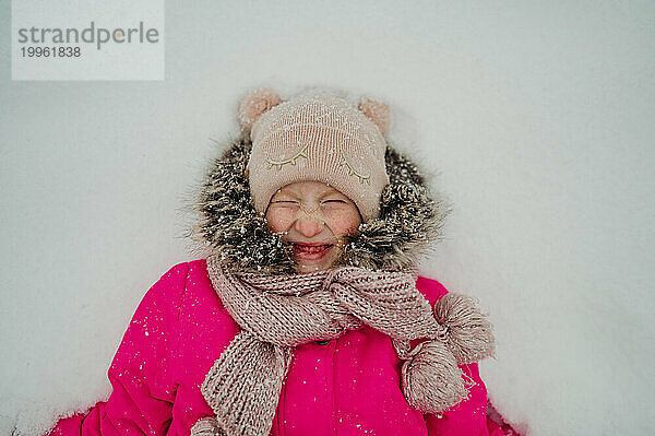 Lächelndes Mädchen  das im Winter auf Schnee liegt