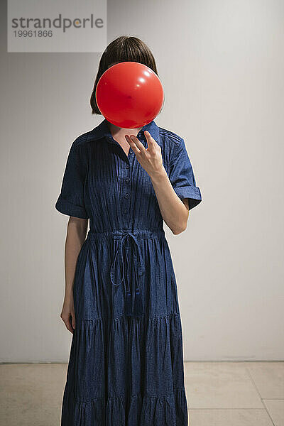 Junge Frau bläst roten Ballon vor der Wand