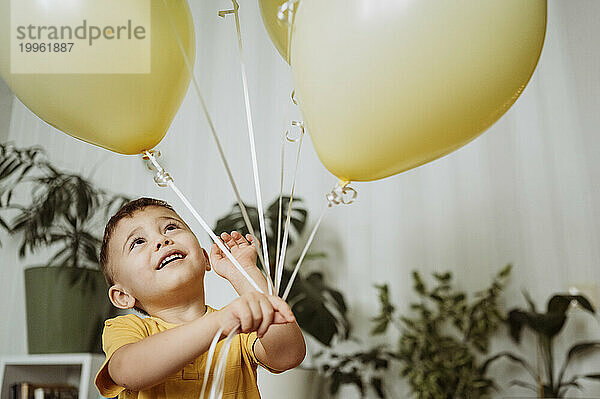 Glücklicher Junge  der zu Hause mit Luftballons spielt