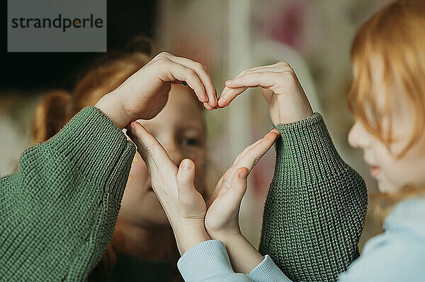 Sisters making heart shape with hands at home