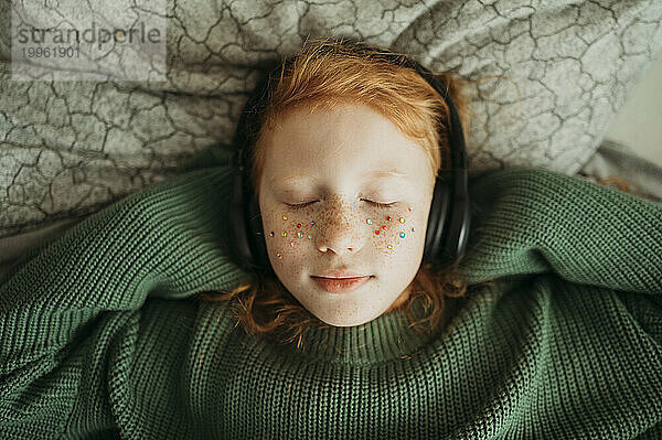 Rothaariges Mädchen hört zu Hause Musik über kabellose Kopfhörer