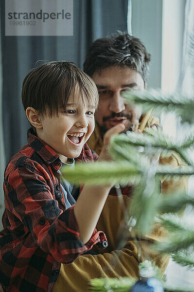 Glücklicher Vater und Sohn schmücken zu Hause den Weihnachtsbaum