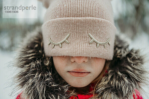 Trauriges Mädchen  das die Augen mit einer rosa Strickmütze bedeckt