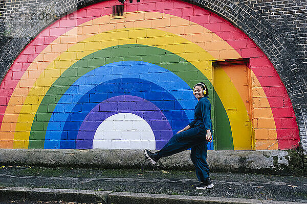 Glückliche Frau mit kabellosen Kopfhörern genießt es vor der Regenbogenwand