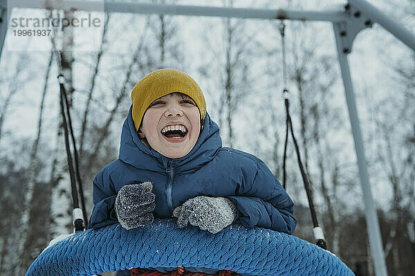 Fröhlicher Junge schwingt und genießt die Reifenschaukel im Winterpark