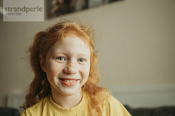 Smiling redhead girl with freckles on face at home