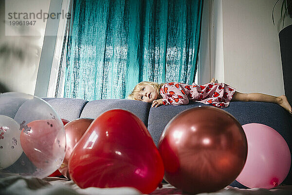 Mädchen liegt zu Hause auf dem Sofa mit Luftballons