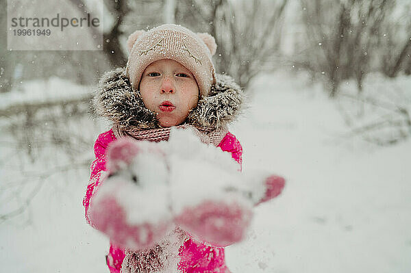 Mädchen bläst im Winterpark auf Schnee