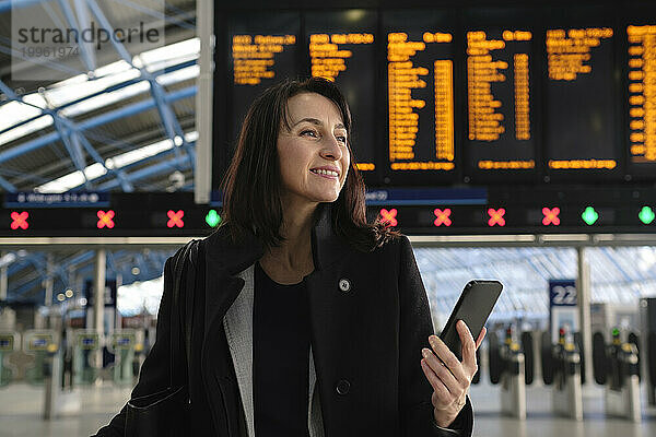 Glückliche Frau mit Handy am Bahnhof