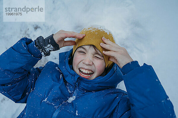 Glücklicher Junge  der im Winter auf Schnee liegt und lacht
