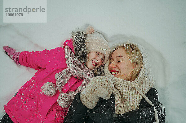 Glückliche Mutter  die mit Tochter im Schnee genießt
