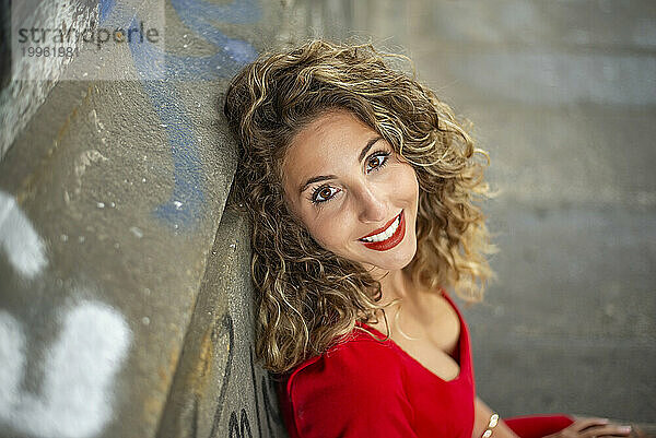 Happy woman with curly hair leaning on wall