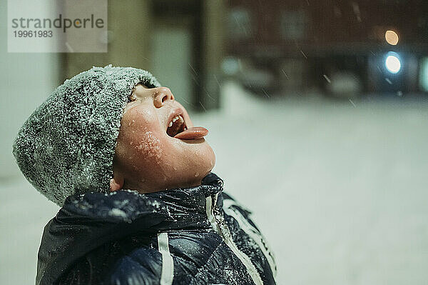 Fröhlicher Junge  der im Winter Schnee mit der Zunge fängt