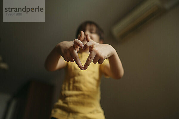 Boy making heart shape with fingers at home