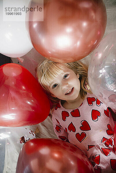 Glückliches Mädchen  das zu Hause inmitten von Luftballons liegt