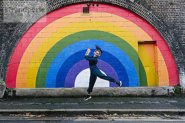 Glückliche Frau springt vor Regenbogenwand