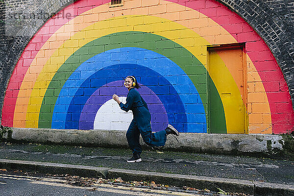 Glückliche junge Frau läuft vor der Regenbogenwand