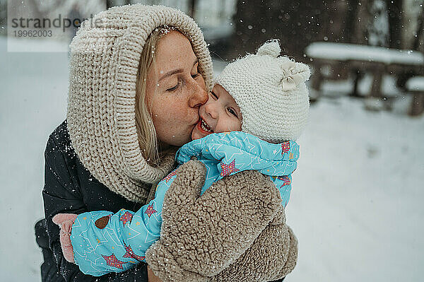 Glückliche Mutter küsst Tochter im Winter