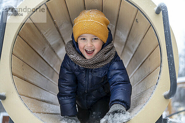 Lächelnder Junge spielt im Tunnel im Winterpark