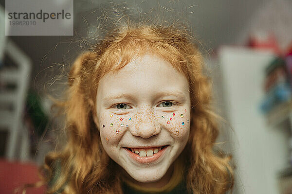 Smiling girl with sequins on face at home