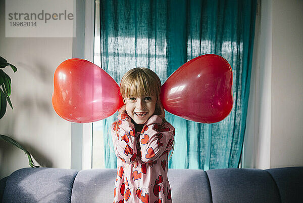 Verspieltes Mädchen hält zu Hause Luftballons über die Ohren