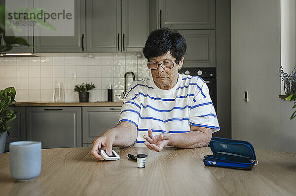Ältere Frau misst Blutzucker mit Glukometer in der Küche
