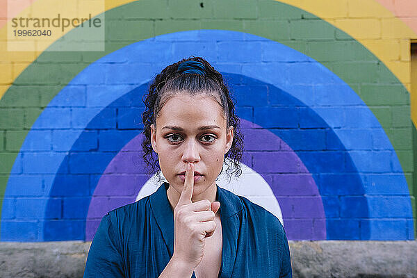 Frau mit Finger auf den Lippen vor der Regenbogenwand