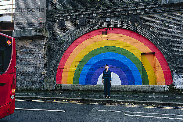 Frau steht vor Regenbogenwand am Fußweg