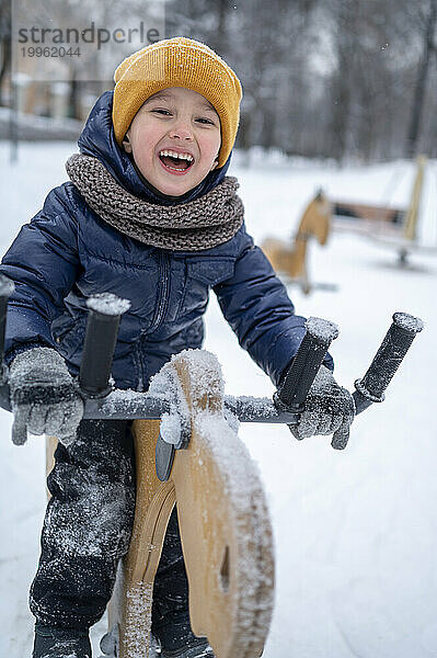 Fröhlicher Junge reitet auf Schaukelpferd im Winterpark