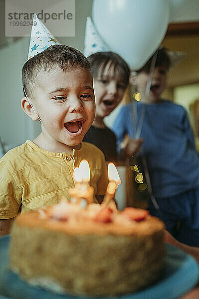 Junge mit offenem Mund bläst zu Hause Geburtstagskerzen auf Kuchen