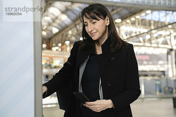 Glückliche Frau kauft Fahrkarte am Automaten am Bahnhof