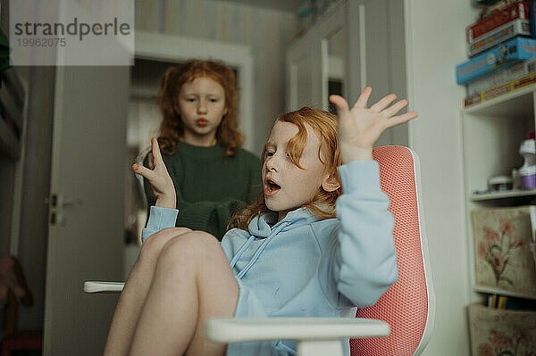 Mädchen sitzt auf einem Stuhl und hat Spaß mit ihrer Schwester im Hintergrund zu Hause