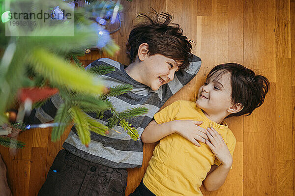 Happy brothers lying on floor under Christmas tree at home