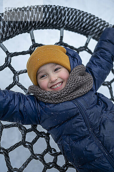 Lächelnder Junge liegt auf Nestschaukel im Winterpark