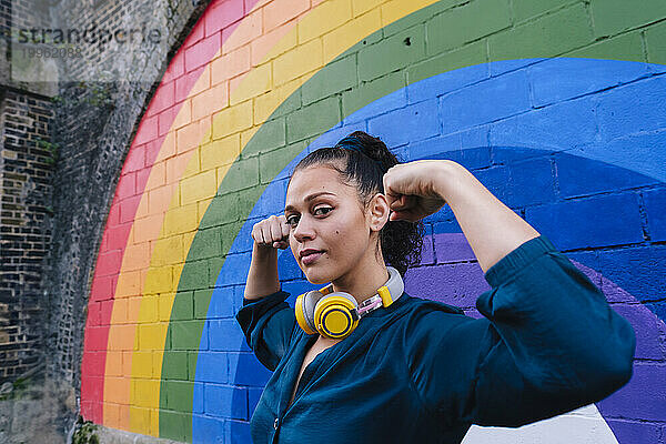 Junge Frau lässt vor der Regenbogenwand Muskeln spielen