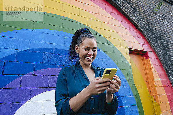 Glückliche junge Frau benutzt Smartphone vor Regenbogenwand