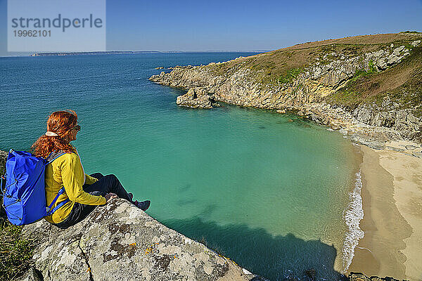 France  Brittany  Female hiker sitting on edge overlooking beach at Cap Sizun headland