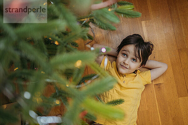 Boy lying on floor under Christmas tree at home