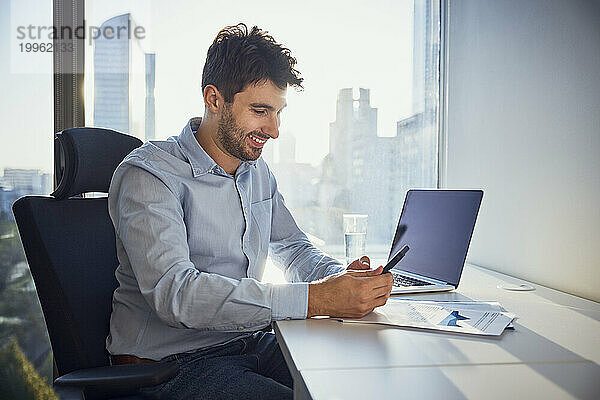 Lächelnder junger Geschäftsmann  der sein Smartphone am Schreibtisch benutzt