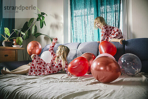 Fröhliche Schwestern spielen zu Hause mit Luftballons auf dem Sofa