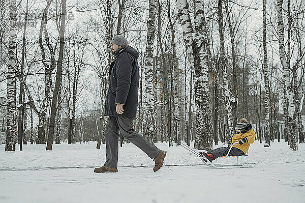 Vater rodelt Sohn auf Schnee im Winterpark